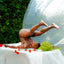 Person in a bubble performing acrobatics with flowers on a white sheet outdoors.