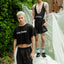 Two people wearing black 'Cake Bandit' clothing standing outdoors with greenery and a building in the background.