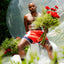 Adair a black trans man wearing striped Cake Bandit Boxers and red shorts holding red flowers with green foliage.