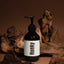 A dark amber pump bottle with a white label reading 'Hunky' Body serum - scar cream in bold black text, styled among rustic driftwood pieces against a warm brown background.