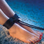 Feet with black rope tied around them on a textured surface, showing Scandal BDSM rope - black