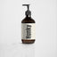 An amber glass pump bottle with a cream label reading 'Hunky' in bold black text, handsome body wash underneath, set on a light marble surface against a clean white background.