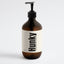 An amber glass pump bottle of Hunky Handmade Body Wash with a black pump and a cream-colored label, set against a plain light gray background.