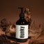 A dark amber pump bottle labeled 'Hunky' Handsome body wash, styled with natural driftwood pieces against a warm brown background.